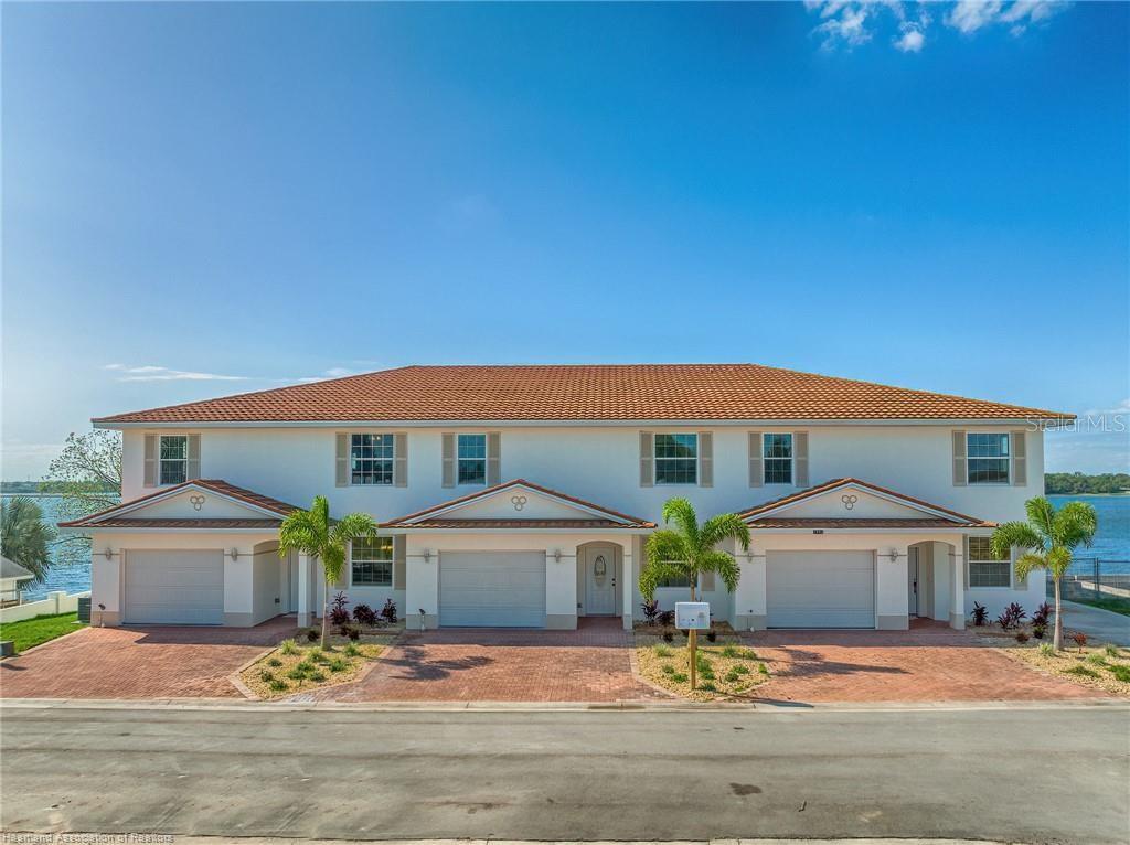 A three-unit townhouse building with white stucco walls, tile roofs, and attached garages — 1900 OASIS BOULEVARD, SEBRING, FL