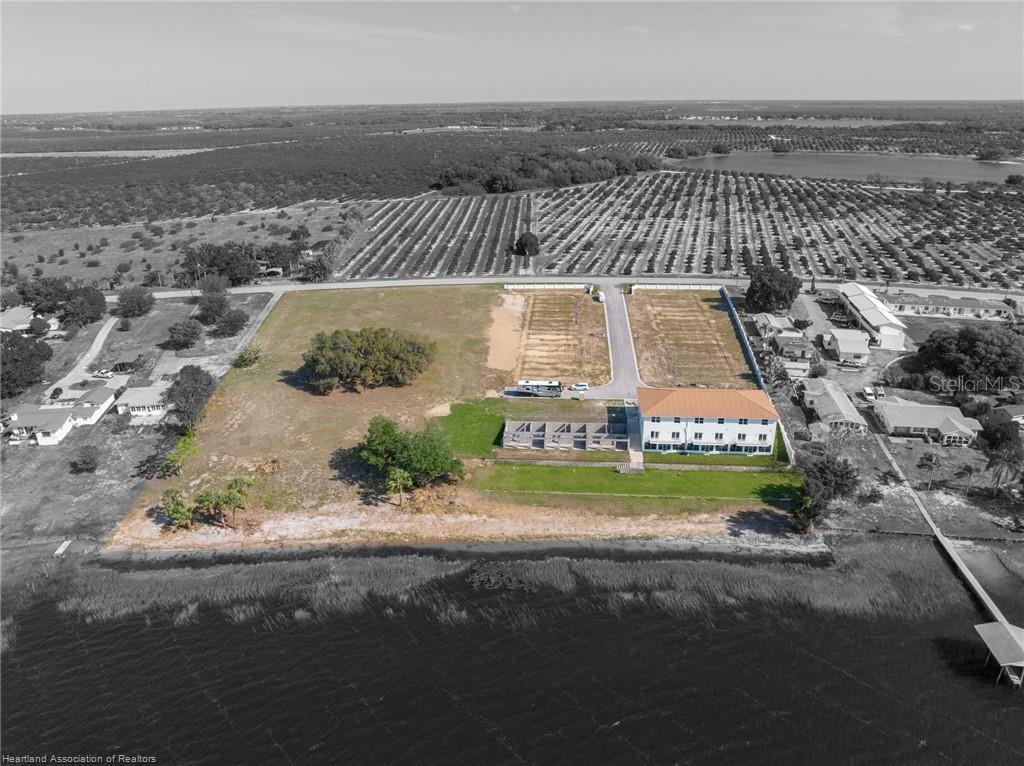 An aerial view shows a multi-story building on a waterfront lot with adjacent cleared land — 1900 OASIS BOULEVARD, SEBRING, FL