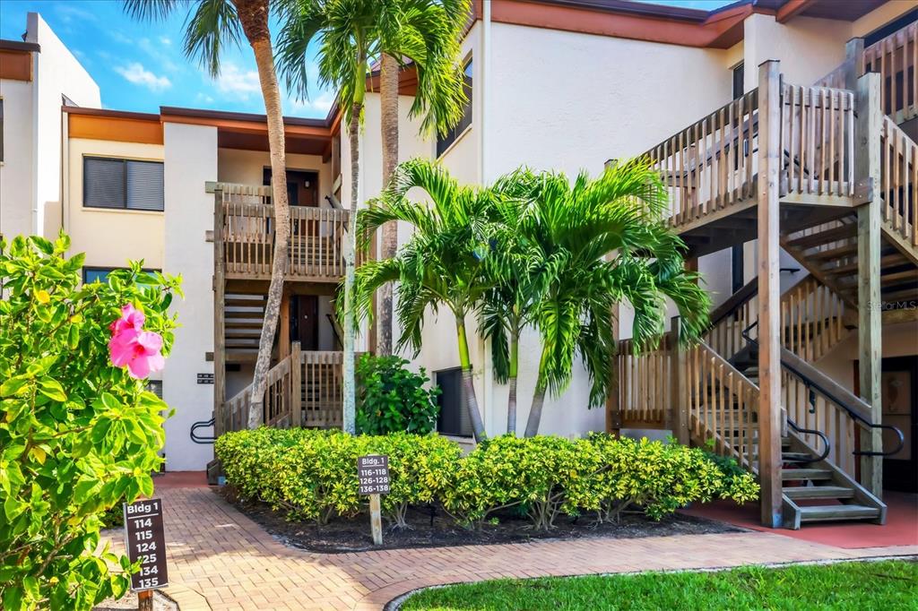 An exterior view of a multi-story apartment building with wooden staircases and tropical landscaping — 1900 COVE II PLACE UNIT 127, SARASOTA, FL