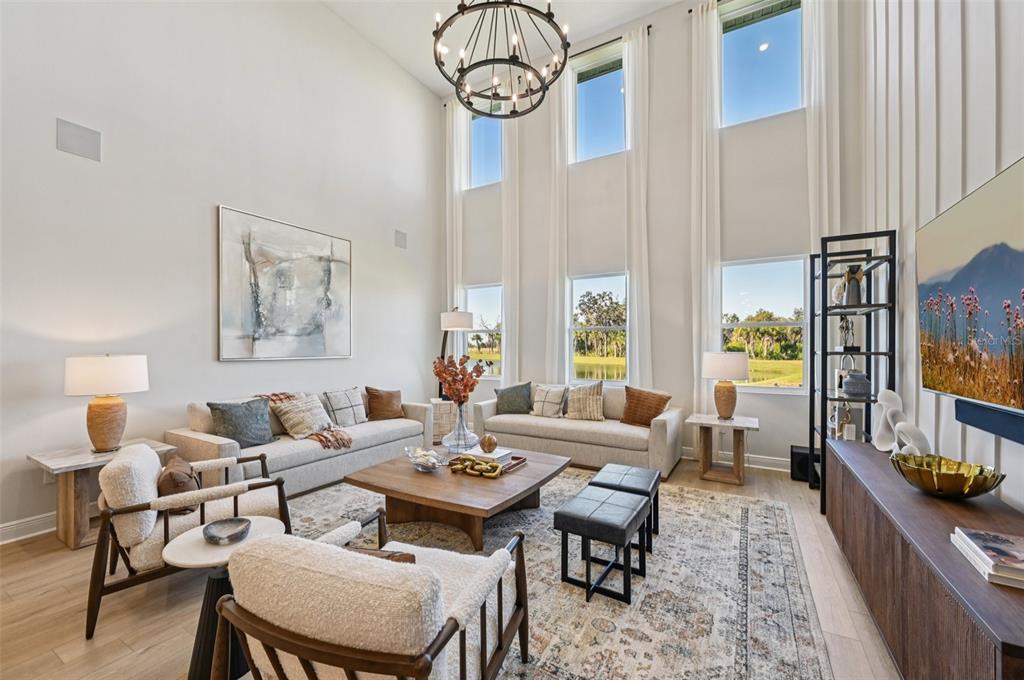 A bright living room features high ceilings, tall windows, a chandelier, and modern neutral furniture — 5977 FRESH FLORA DRIVE, WIMAUMA, FL