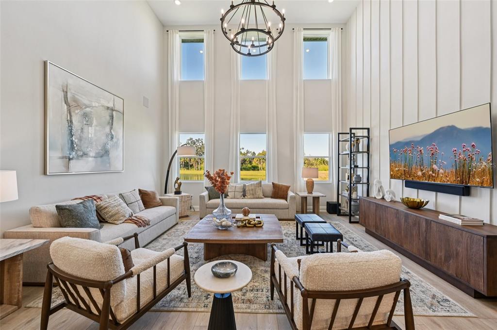 A bright living room features high ceilings, tall windows, two sofas, and a central chandelier — 5977 FRESH FLORA DRIVE, WIMAUMA, FL