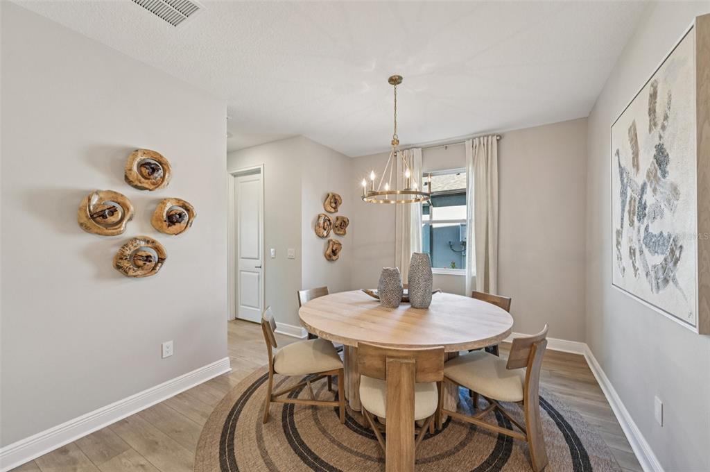 A bright, high-ceilinged living room features a large chandelier, floor-to-ceiling windows, and modern furniture — 5977 FRESH FLORA DRIVE, WIMAUMA, FL