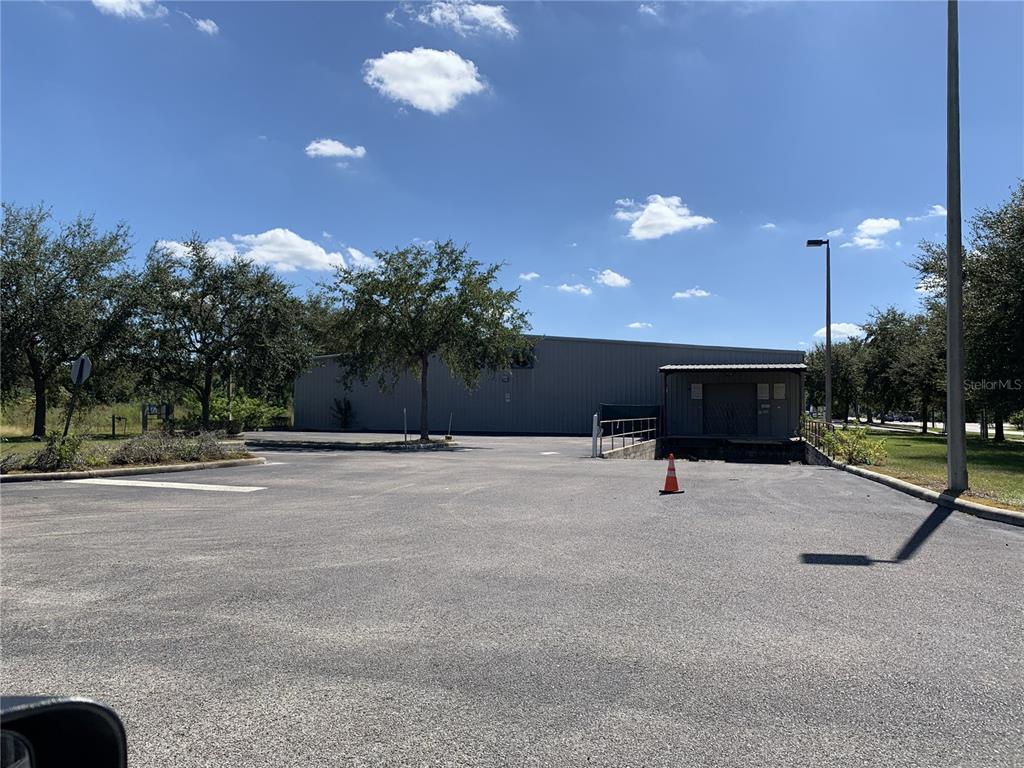 A large metal warehouse building sits behind a paved parking lot under a blue sky — 1510 E COLLEGE AVENUE, RUSKIN, FL