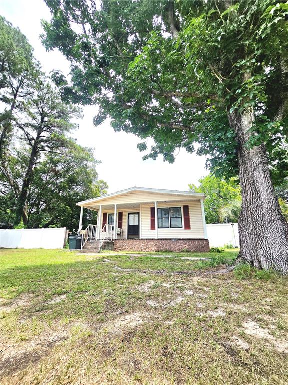 A single-story house with light siding, red shutters, and a front porch under large trees — 3265 SE 132ND PLACE, BELLEVIEW, FL