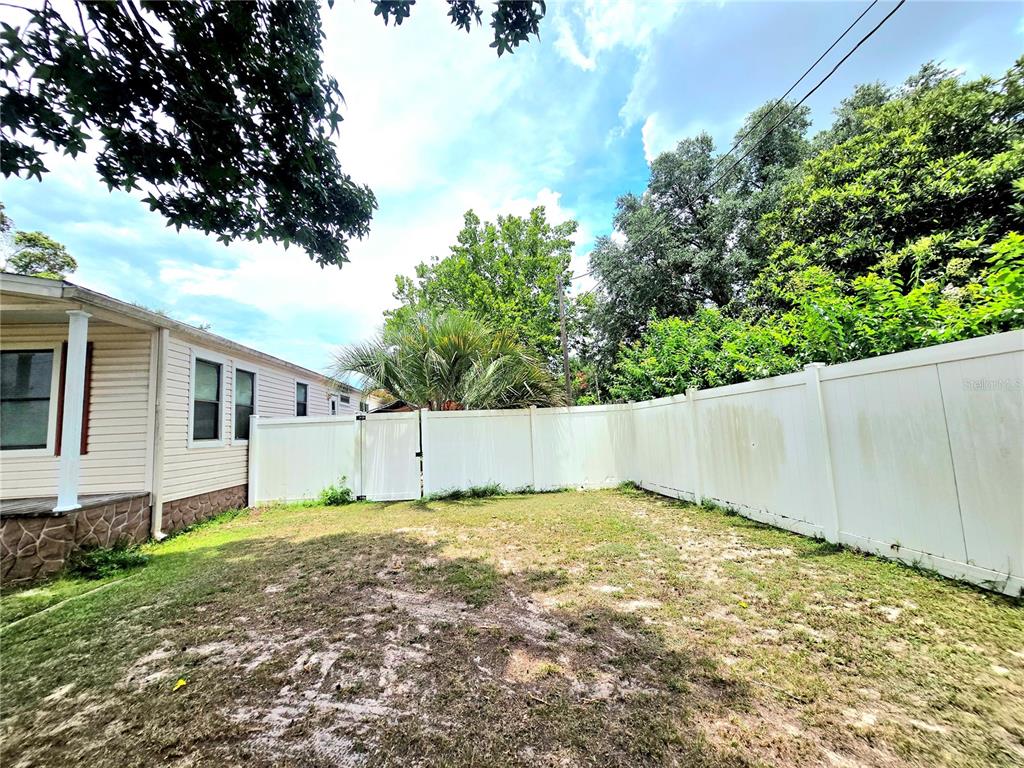 A fenced backyard with a grassy lawn and a side view of a house — 3265 SE 132ND PLACE, BELLEVIEW, FL