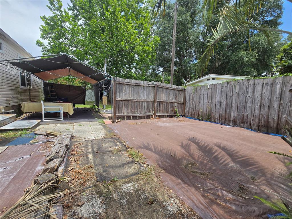 A backyard features a wooden fence, a covered patio area, and a brown ground covering — 3265 SE 132ND PLACE, BELLEVIEW, FL