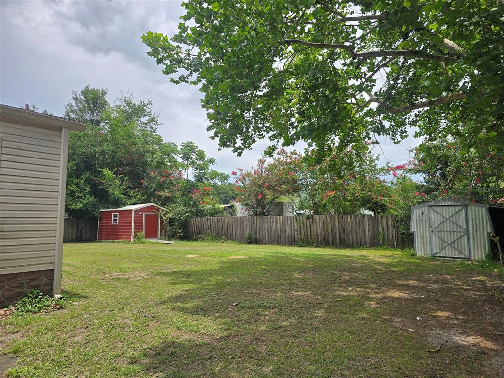 A grassy backyard features two storage sheds, a wooden fence, and mature trees — 3265 SE 132ND PLACE, BELLEVIEW, FL