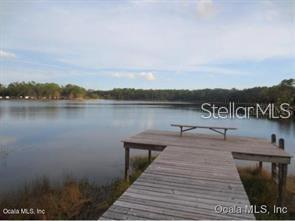 A wooden dock with a bench extends into a calm lake surrounded by trees — 7TH LOOP, SILVER SPRINGS, FL