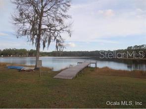 A wooden dock extends into a calm lake from a grassy shore with a large tree — 7TH LOOP, SILVER SPRINGS, FL