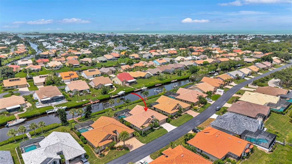 An aerial view shows a residential neighborhood with houses, a canal, and a red arrow — 103 INLETS BOULEVARD UNIT 103, NOKOMIS, FL