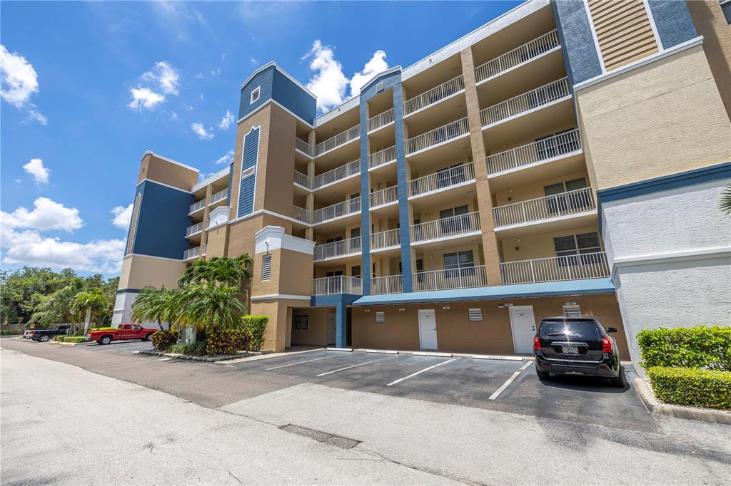 A multi-story apartment building features balconies, covered ground-level parking, and a paved driveway — 960 STARKEY ROAD UNIT 2202, LARGO, FL