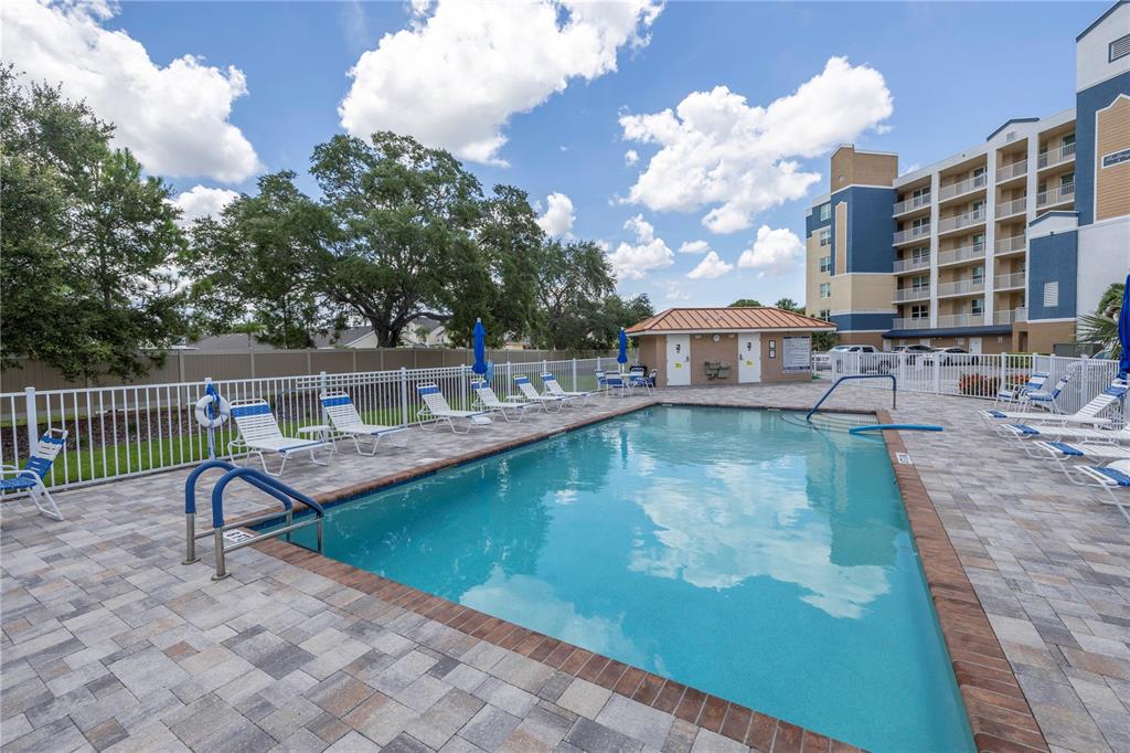 An outdoor swimming pool with lounge chairs on a paved deck beside a multi-story building — 960 STARKEY ROAD UNIT 2202, LARGO, FL