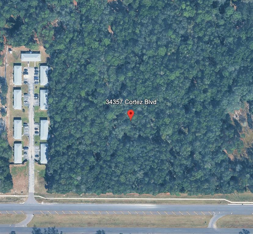 This aerial view shows a wooded lot adjacent to a residential complex and a highway — 34357 CORTEZ BOULEVARD, DADE CITY, FL