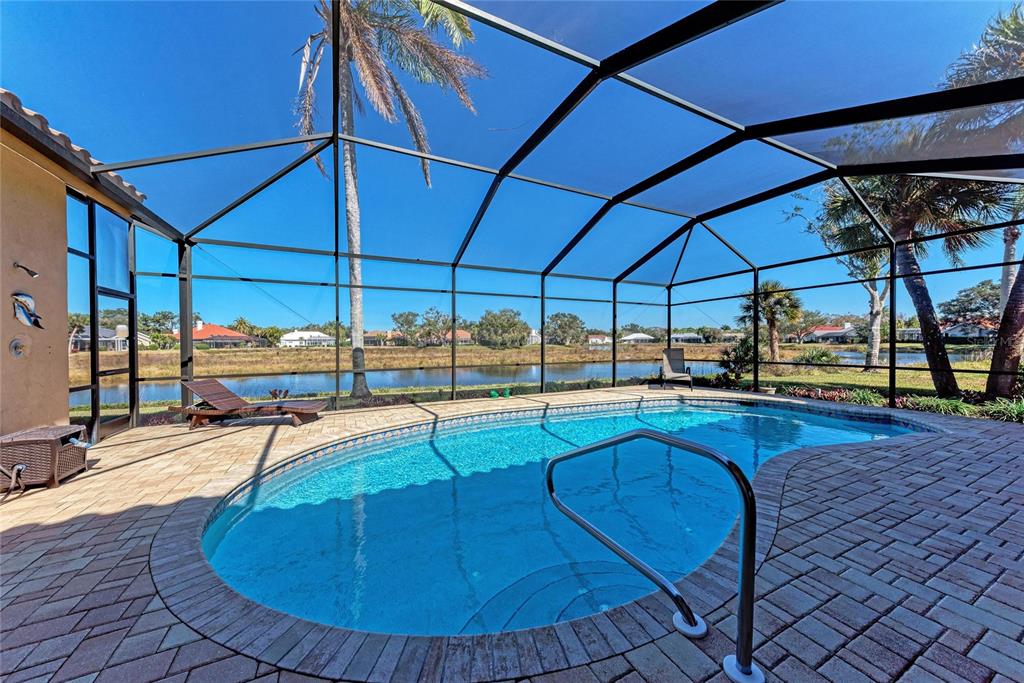 A screened-in patio features a swimming pool, brick pavers, and a view of a pond — 8383 CYPRESS HOLLOW DRIVE, SARASOTA, FL