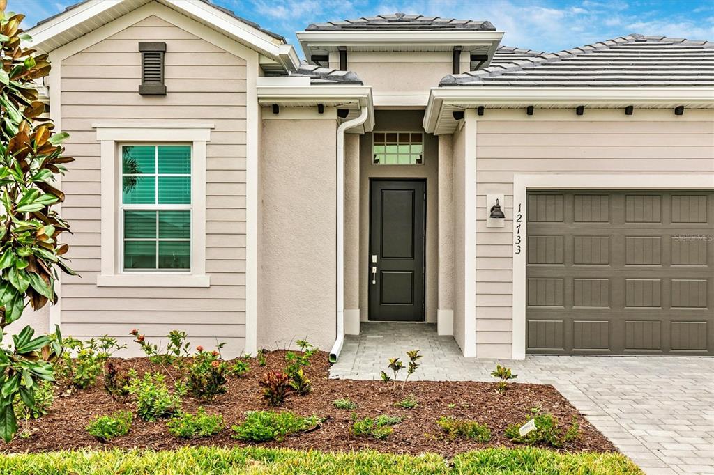 The exterior of a single-story house features beige siding, a dark front door, and a garage — 12733 TULUM LOOP, VENICE, FL