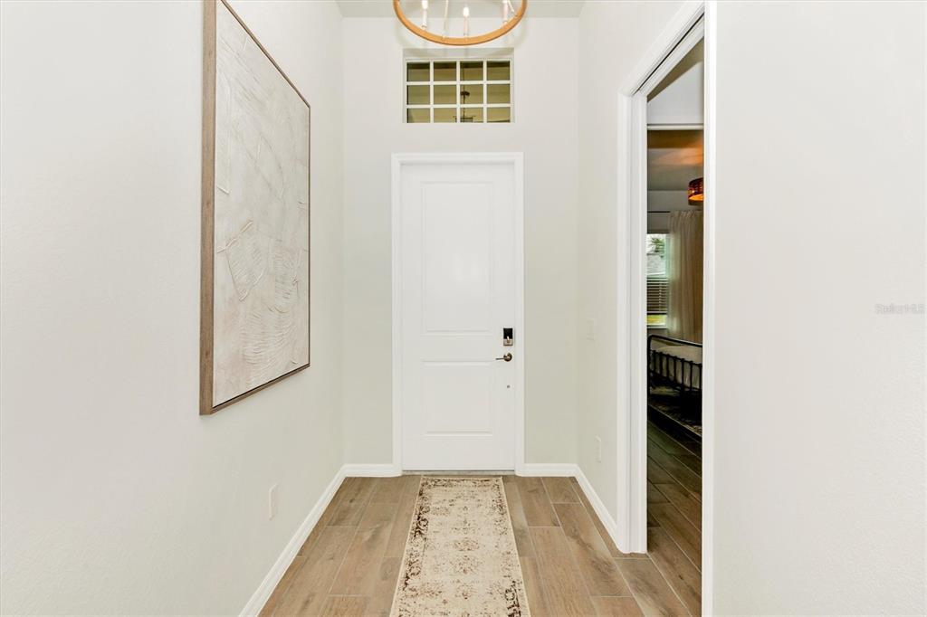 A bright entryway features a white door, a transom window, and wood-look tile flooring — 12733 TULUM LOOP, VENICE, FL