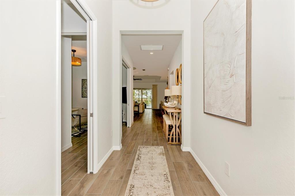 A hallway with wood-look tile flooring leads to an open living area with a view — 12733 TULUM LOOP, VENICE, FL