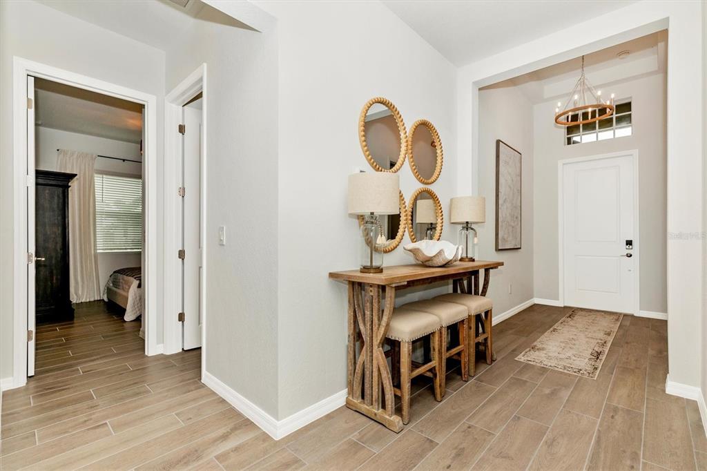 A bright entryway features wood-look tile flooring, a rustic console table, and a white door — 12733 TULUM LOOP, VENICE, FL