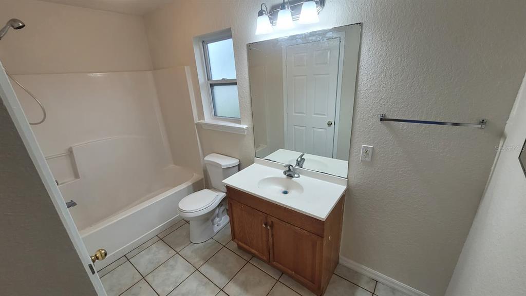 A bathroom features a tub-shower combination, a wood vanity with a sink, and tile flooring — 323 W 9TH STREET, LAKELAND, FL