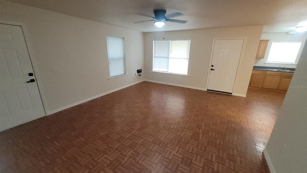 An open-concept living room features wood-look flooring, a ceiling fan, and an adjacent kitchen area — 323 W 9TH STREET, LAKELAND, FL