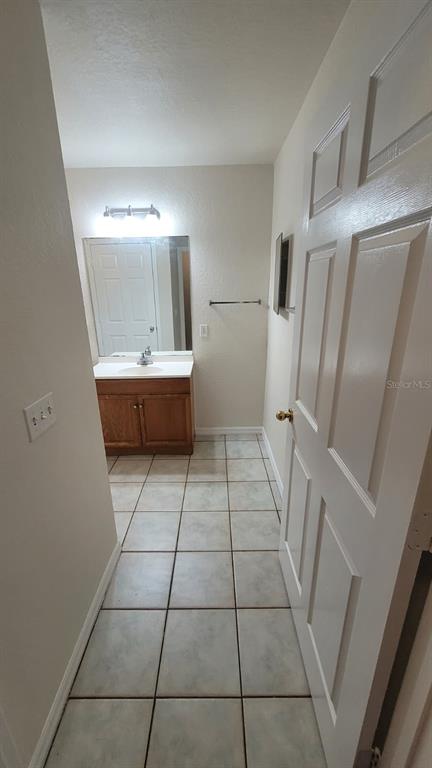 A bathroom with a wooden vanity, a mirror, and light-colored tiled flooring — 323 W 9TH STREET, LAKELAND, FL