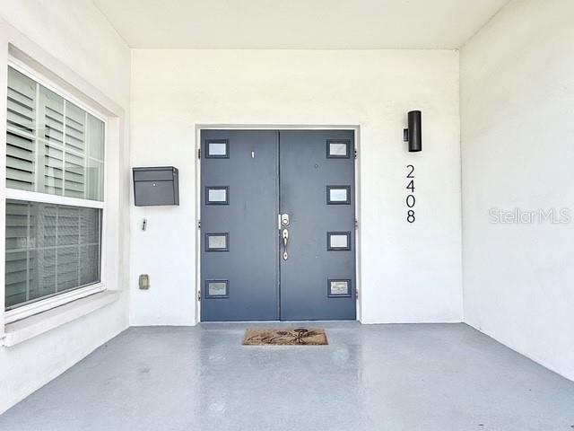 A covered entryway features a gray double door, a wall-mounted mailbox, and house numbers — 2408 CORRINE DRIVE, ORLANDO, FL