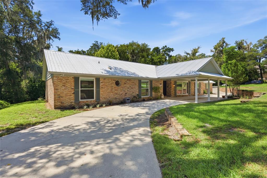 A single-story brick house with a metal roof and a concrete driveway under a carport — 1150 MARKHAM WOODS ROAD, LONGWOOD, FL