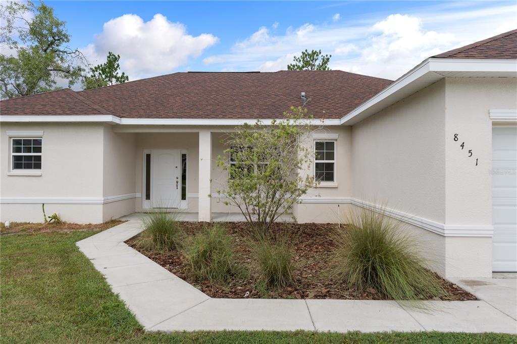 The front exterior of a single-story house features a tan stucco facade, a covered entryway, and landscaping — 8451 NUZUM ROAD, WEEKI WACHEE, FL