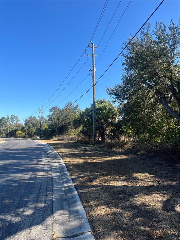 A paved road curves past a grassy lot with utility poles and trees — E SKLAR DRIVE, VENICE, FL