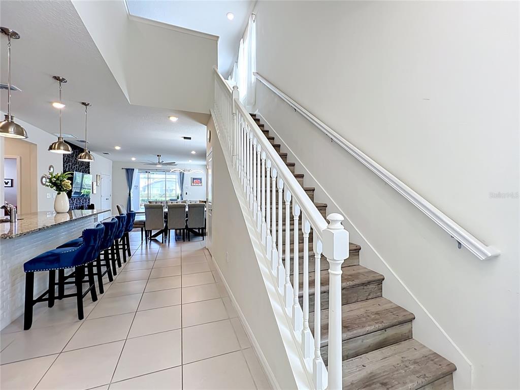 A staircase with wood-look treads and white railings sits beside a kitchen island with stools — 4033 LANA AVENUE, DAVENPORT, FL