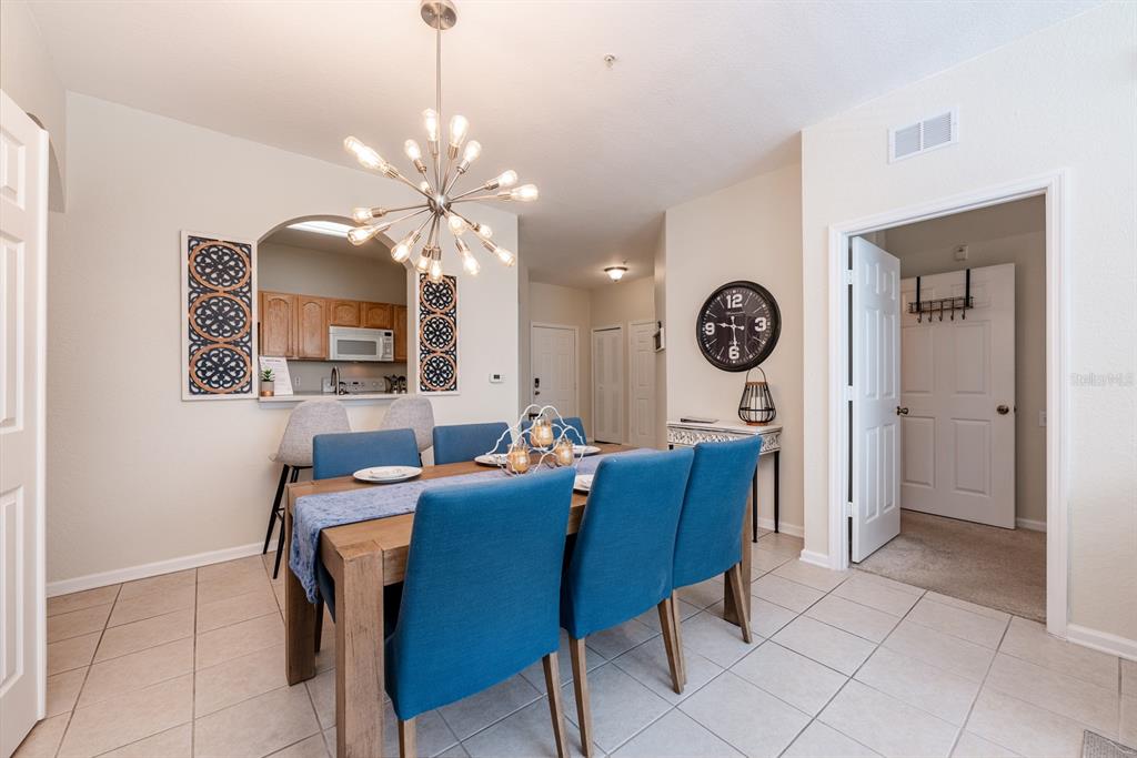 A dining room features a wooden table with blue chairs, a chandelier, and kitchen pass-through — 2778 ALMATON LOOP UNIT 204, KISSIMMEE, FL