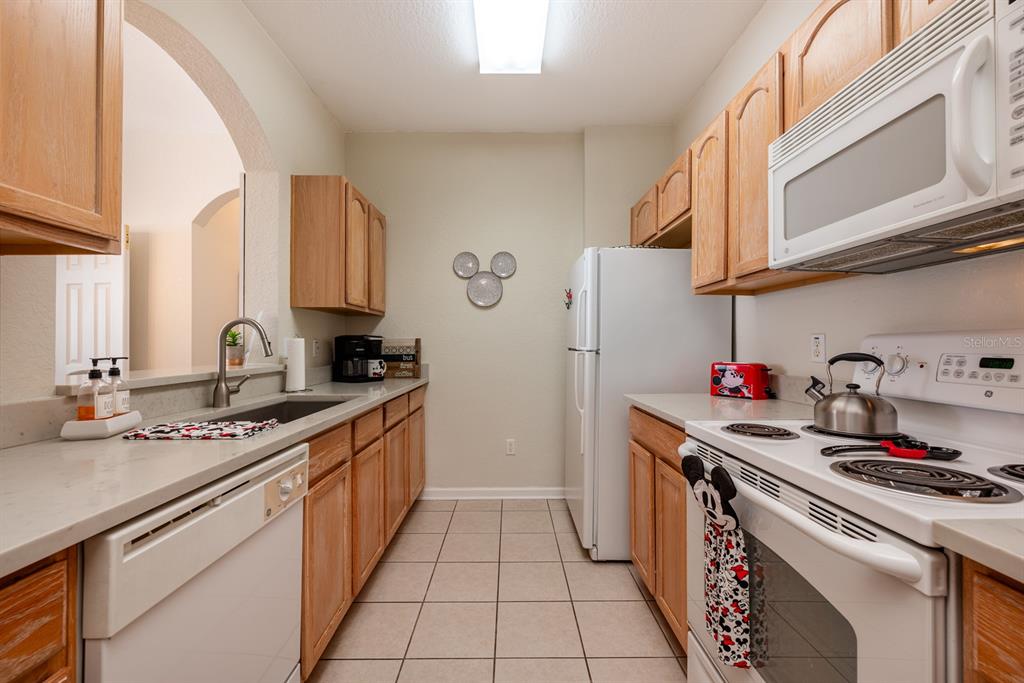 A galley kitchen features light wood cabinets, white appliances, tile flooring, and a Mickey Mouse theme — 2778 ALMATON LOOP UNIT 204, KISSIMMEE, FL