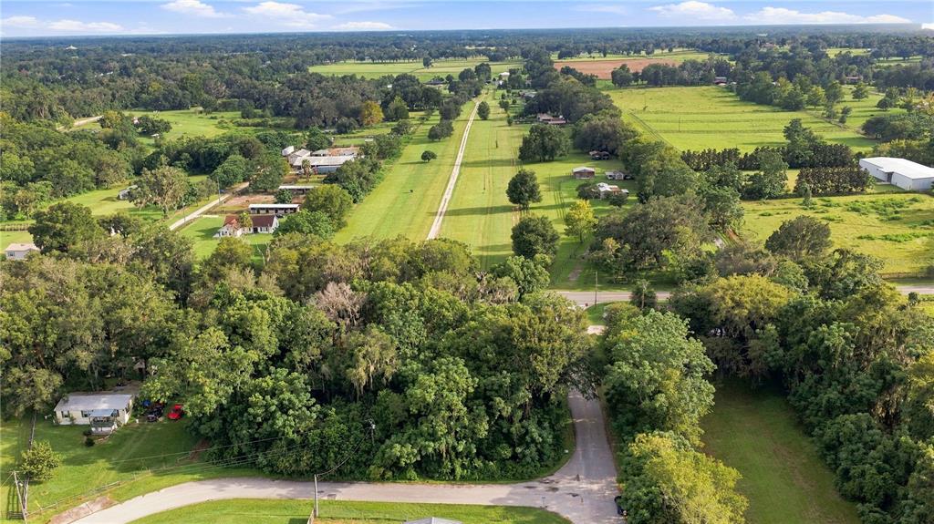 An aerial view shows a rural landscape with houses, trees, and a long grassy path — 5850 SE 144TH PLACE, SUMMERFIELD, FL