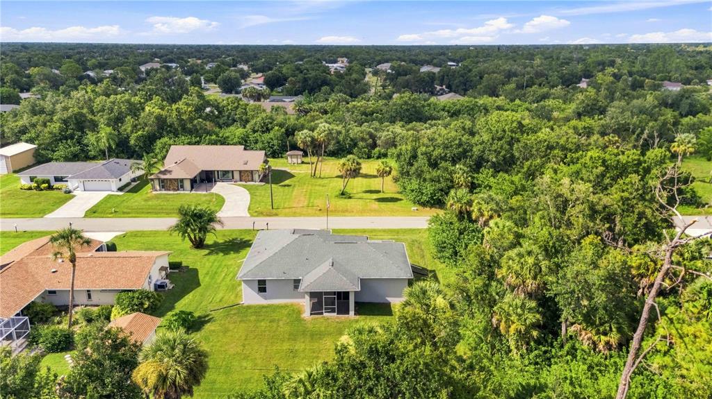 An aerial view shows a residential neighborhood with several houses, green lawns, and dense trees — 22437 ADORN AVENUE, PORT CHARLOTTE, FL