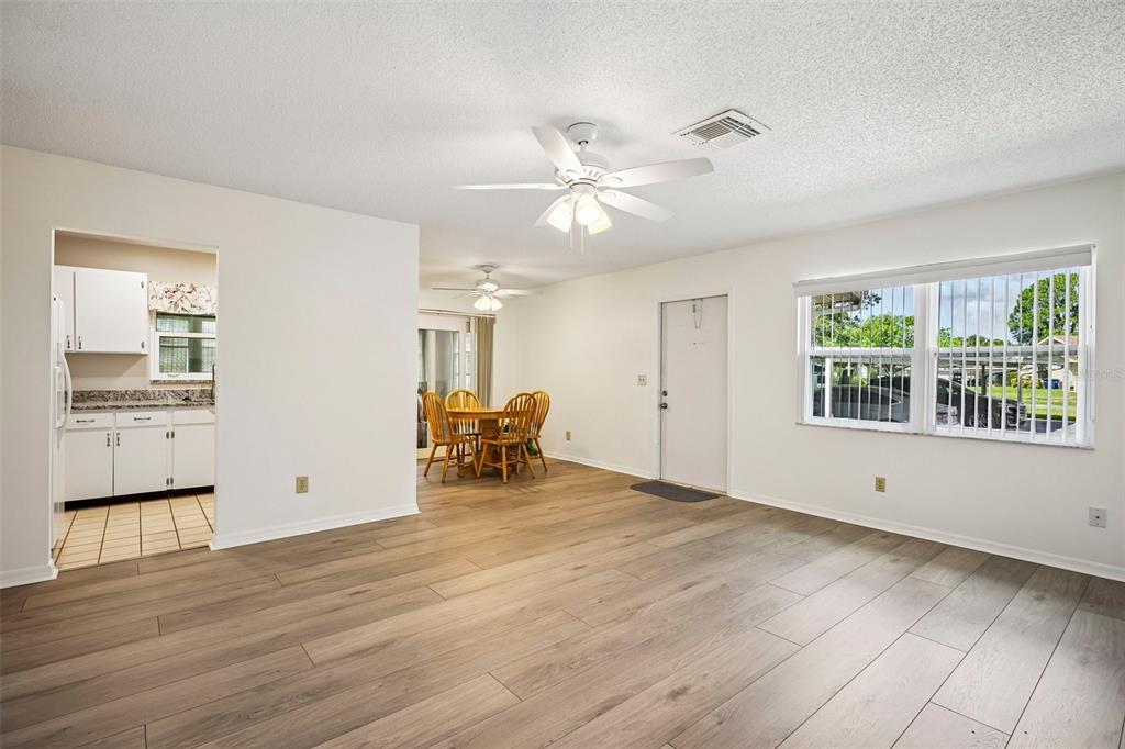 A living room with wood-look flooring, a ceiling fan, and an adjacent kitchen and dining area — 2224 GRENADIER DRIVE, SUN CITY CENTER, FL