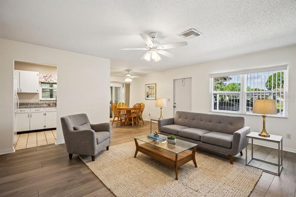 A living room with gray furniture, a glass coffee table, and an adjacent dining area — 2224 GRENADIER DRIVE, SUN CITY CENTER, FL