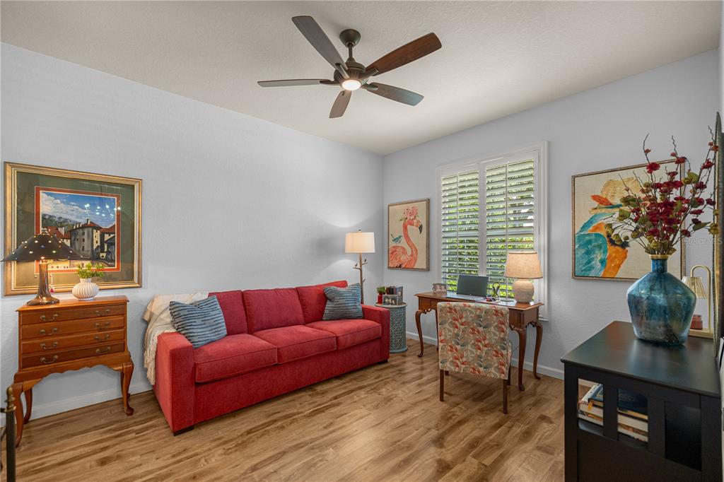 A room with a red sofa, a wooden desk, and a ceiling fan on wood floors — 9383 SW 71ST LOOP, OCALA, FL