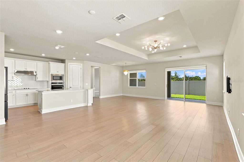 An open-concept kitchen and living area features white cabinetry, light wood floors, and sliding doors — 1803 GROVELINE ROAD, ST CLOUD, FL