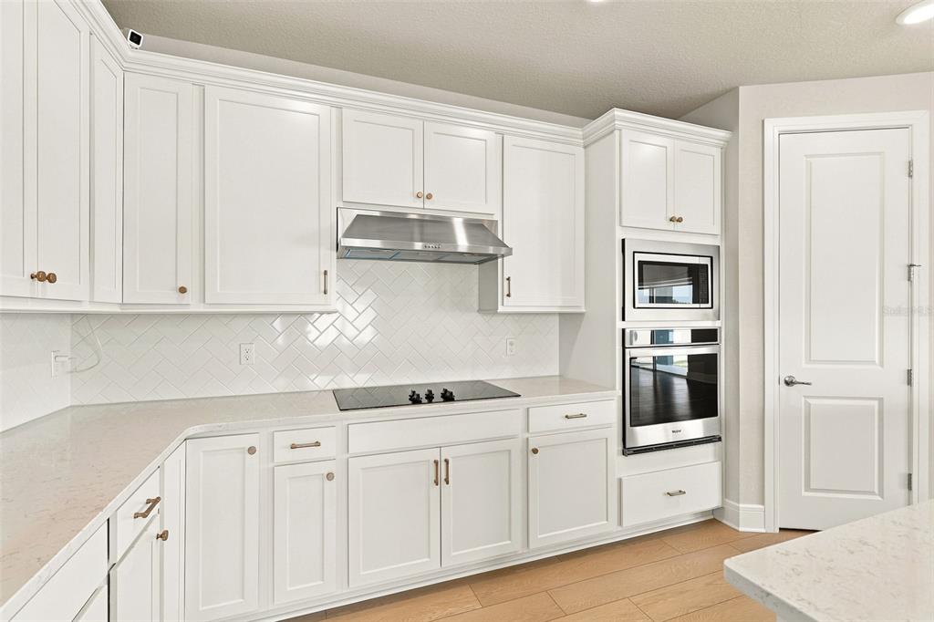 A kitchen features white cabinetry, stainless steel appliances, a herringbone tile backsplash, and quartz countertops — 1803 GROVELINE ROAD, ST CLOUD, FL