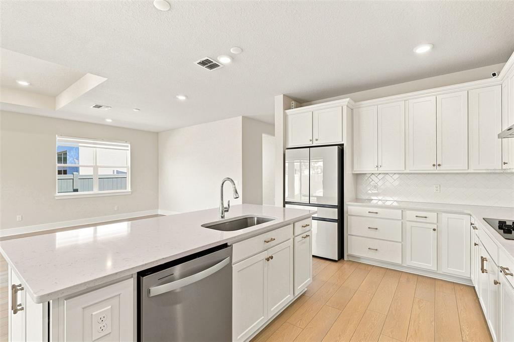 A modern kitchen features white cabinets, a large quartz island with a sink, and light flooring — 1803 GROVELINE ROAD, ST CLOUD, FL