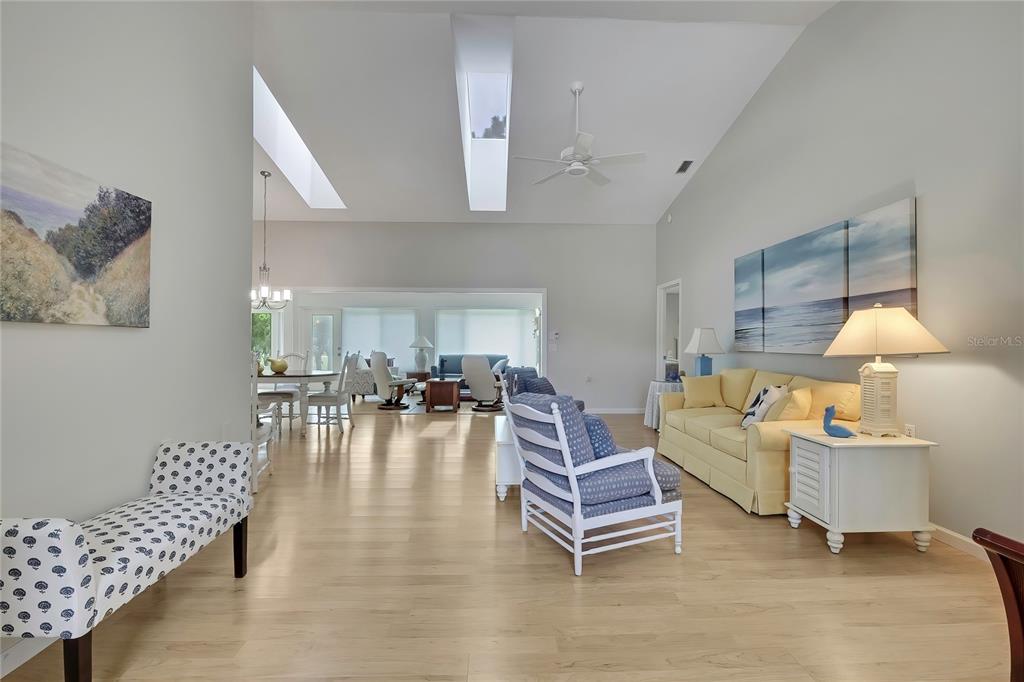 A spacious living room features vaulted ceilings with skylights, light wood flooring, and coastal decor — 2356 ROLLING VIEW DRIVE, SPRING HILL, FL