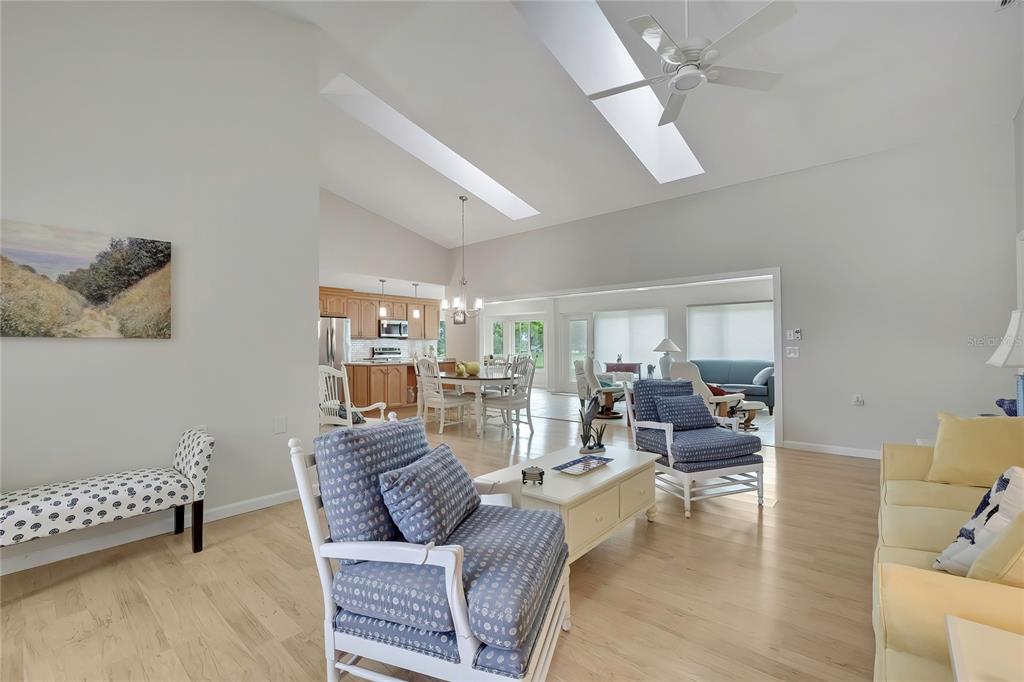 A living room with light wood floors, vaulted ceilings with skylights, and an adjacent kitchen — 2356 ROLLING VIEW DRIVE, SPRING HILL, FL