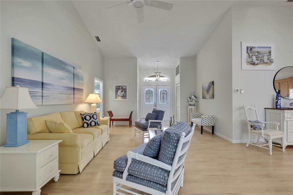 A bright living room features a yellow sofa, patterned armchairs, and light wood flooring — 2356 ROLLING VIEW DRIVE, SPRING HILL, FL