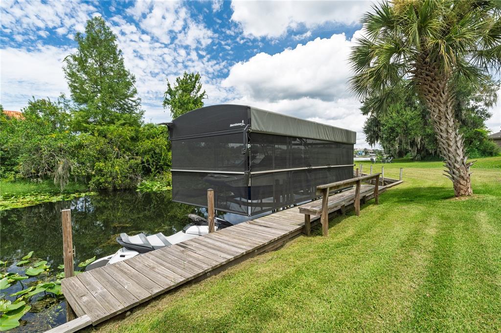 A wooden dock extends along a canal toward a covered boat lift with mesh screens — 2260 W CLASSIC COURT, LONGWOOD, FL