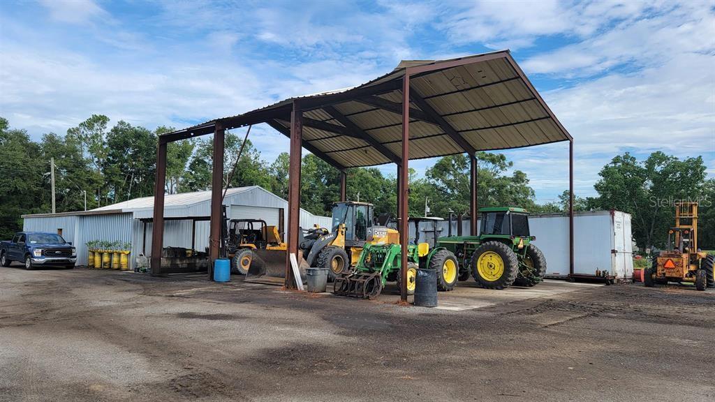 An open-sided metal equipment shed houses several tractors and construction vehicles on a gravel lot — 26208 COUNTY ROAD 49, O'BRIEN, FL