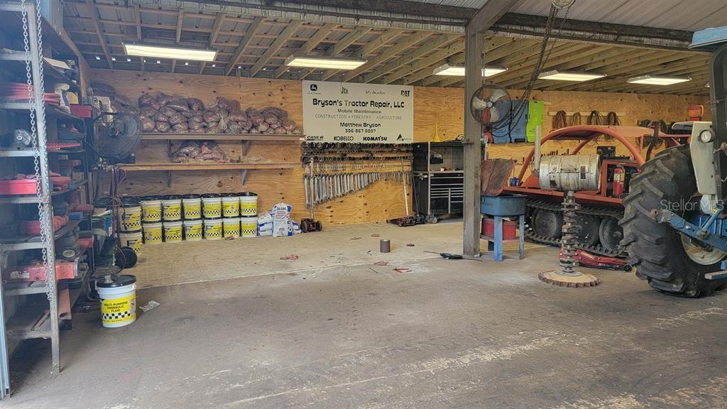 A spacious workshop features a large tractor, organized tool racks, and multiple storage shelves — 26208 COUNTY ROAD 49, O'BRIEN, FL
