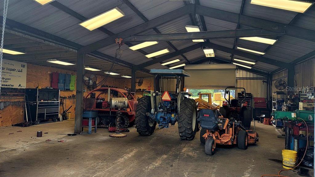 A large, open-concept metal workshop contains tractors, lawn mowers, and various mechanical tools — 26208 COUNTY ROAD 49, O'BRIEN, FL