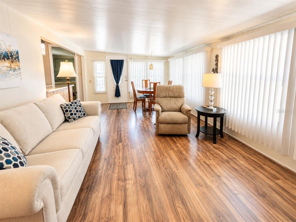 A living room with wood-look flooring, a beige sofa, a recliner, and vertical window blinds — 6921 MARLIN LANE, BRADENTON, FL