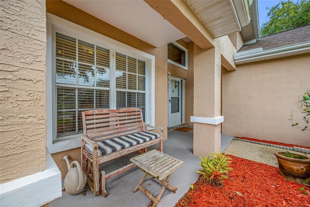 A covered front porch features a wooden bench, a small table, and red mulch landscaping — 1044 DALESIDE LANE, NEW PORT RICHEY, FL