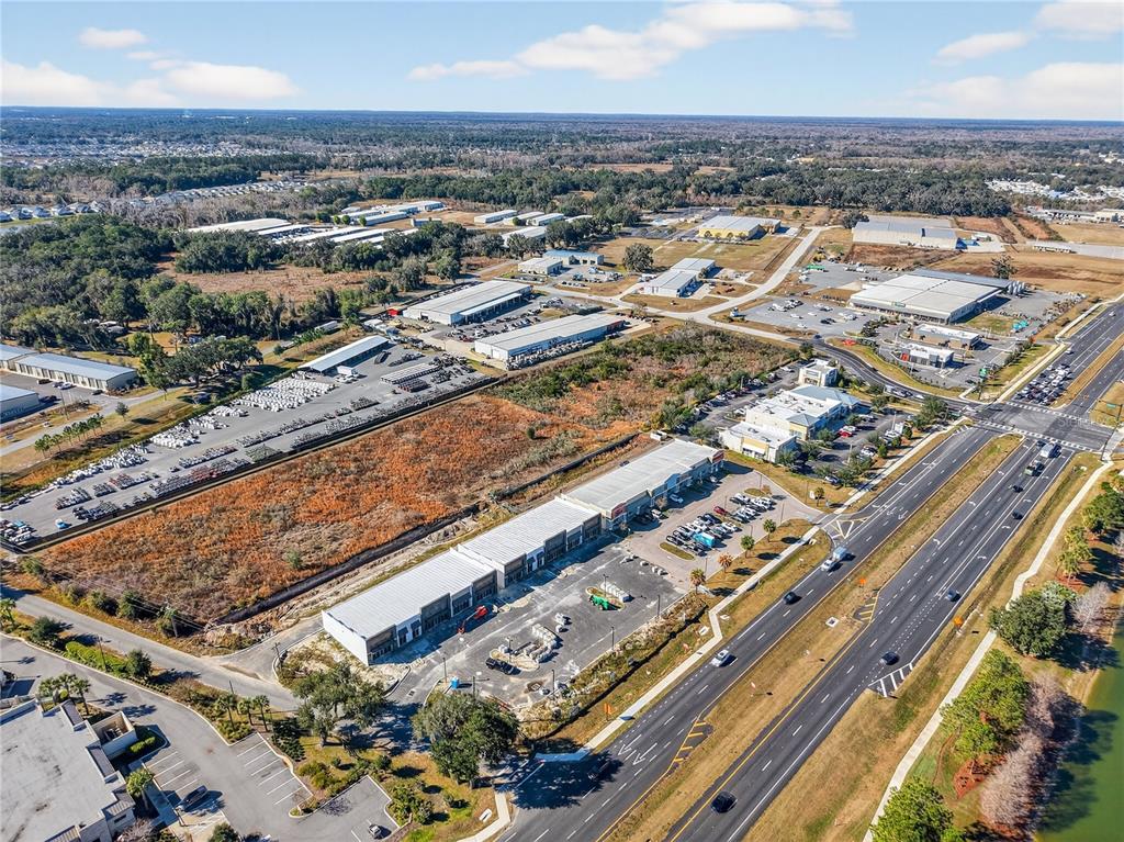 An aerial view shows a commercial strip center, industrial warehouses, and a multi-lane highway — 4713 E STATE ROAD 44, WILDWOOD, FL